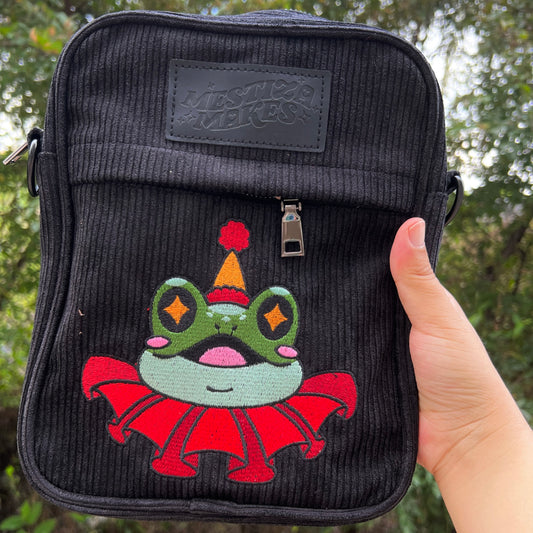 A black corduroy crossbody side bag with an embroidered clown frog design, featuring a removable strap and metal hardware.