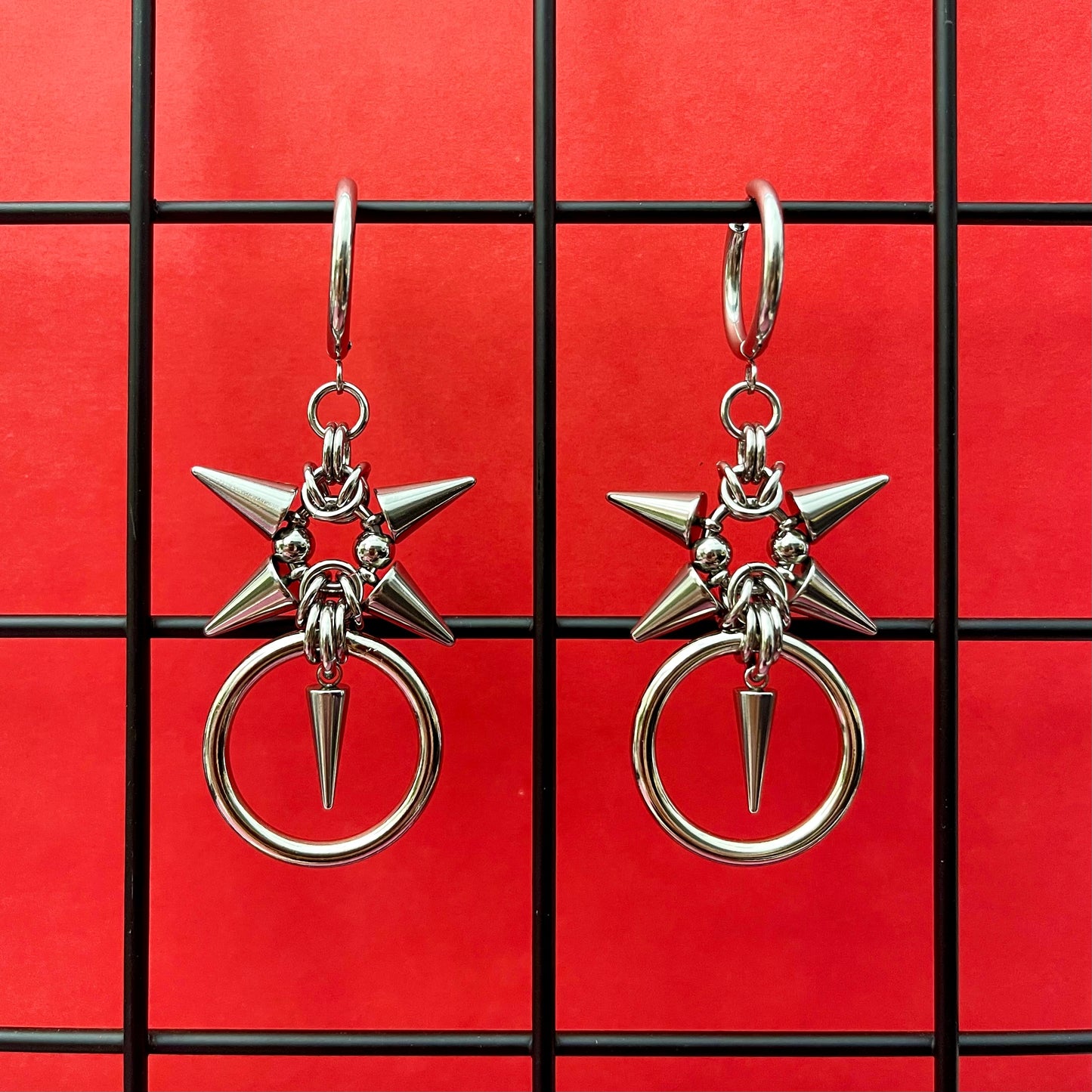 A pair of stainless steel spiky earrings with a heavy o-ring on a red background.